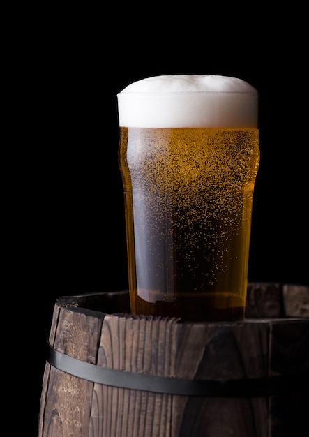 Bicchiere freddo di birra artigianale sul vecchio barilotto di legno su sfondo nero
