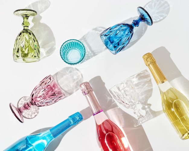 Bicchieri colorati per vino e bottiglia con spumante giallo rosa e blu su tavola bianca