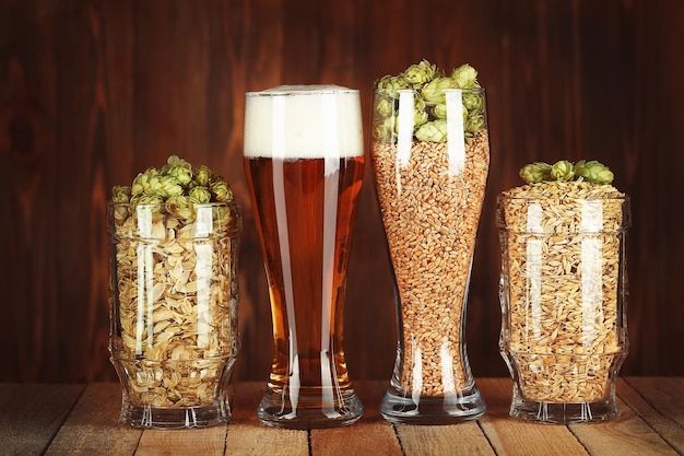 Bicchieri con birra luppolo e malti su sfondo di legno