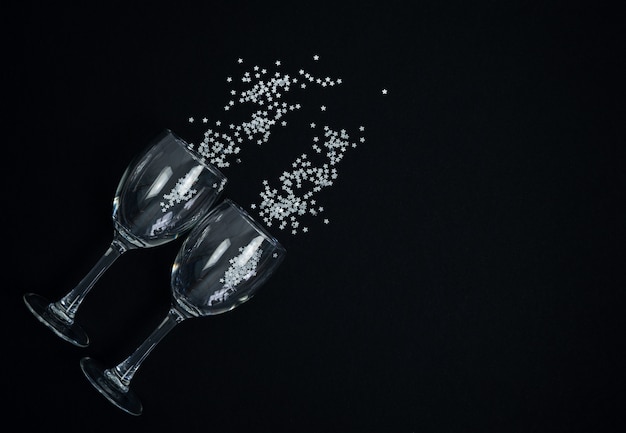 Bicchieri da vino con coriandoli argento su sfondo nero.