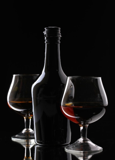 Bicchieri di brandy e bottiglia su sfondo nero