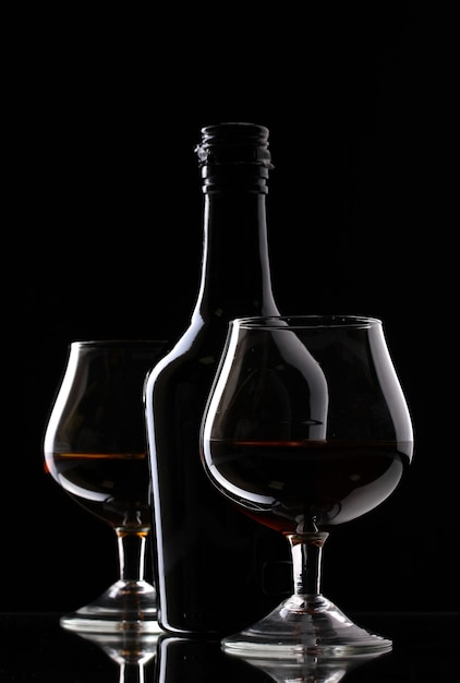 Bicchieri di brandy e bottiglia su sfondo nero
