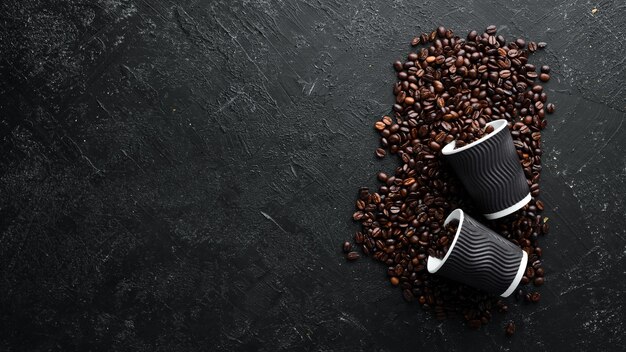 Bicchieri di carta per caffè e chicchi di caffè su sfondo di pietra nera Vista dall'alto Spazio libero per il testo