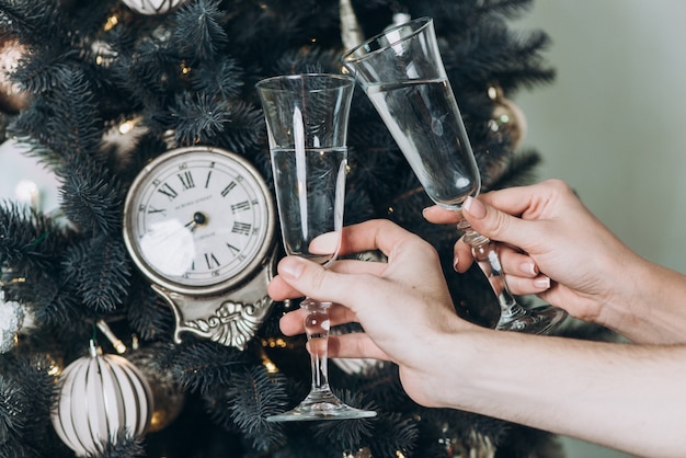 Bicchieri di champagne nelle mani su uno sfondo di albero di Natale