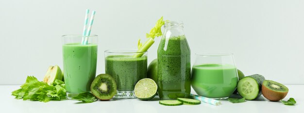 Bicchieri di frullato verde e ingredienti sul tavolo bianco