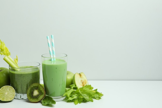 Bicchieri di frullato verde e ingredienti sul tavolo bianco