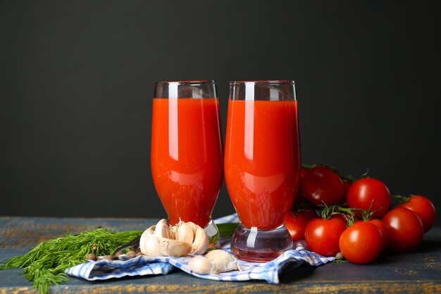 Bicchieri di gustoso succo di pomodoro e pomodori freschi sul tavolo su sfondo grigio