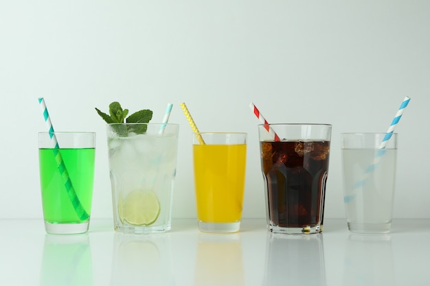 Bicchieri di soda differenti isolati su superficie bianca