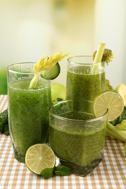 Bicchieri di succo di verdura verde e verdure sulla tovaglia su sfondo luminoso