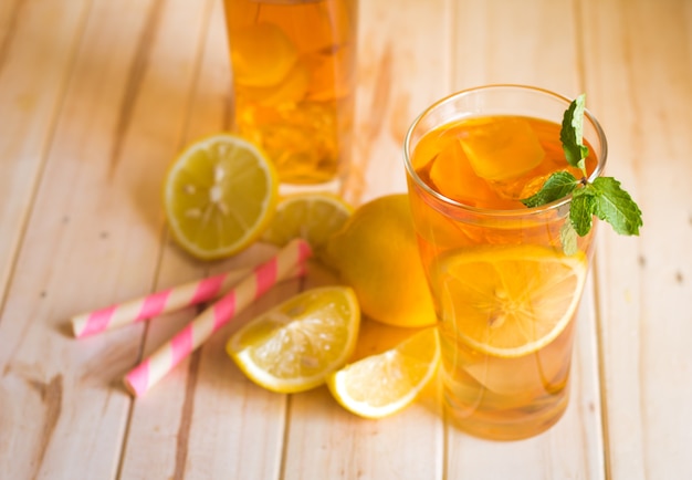 Bicchieri di tè freddo con fette di limone e menta su fondo di legno