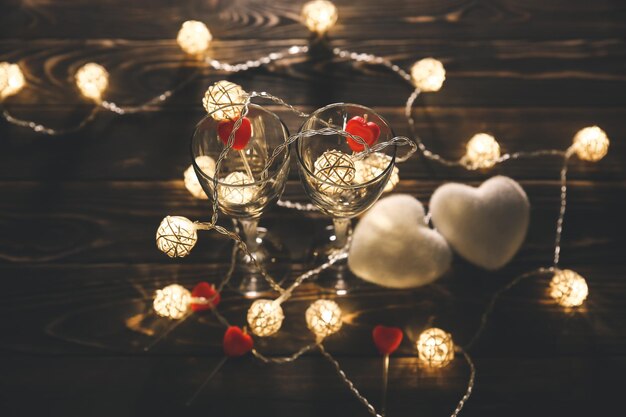 Bicchieri di vino romantici con cuori per il giorno di San Valentino Appuntamento romantico e cena Luci accoglienti Fondo in legno Cartolina di vacanza Concetto di amore