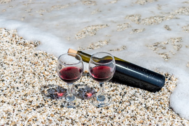 Bicchieri di vino rosso e bottiglia sulla spiaggia durante la giornata di sole estivo