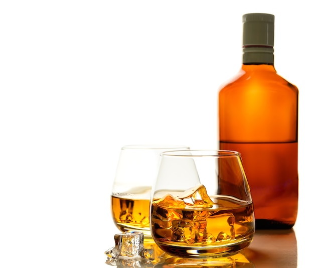 Bicchieri di whisky con ghiaccio e bottiglia di whisky su sfondo bianco. Messa a fuoco selettiva