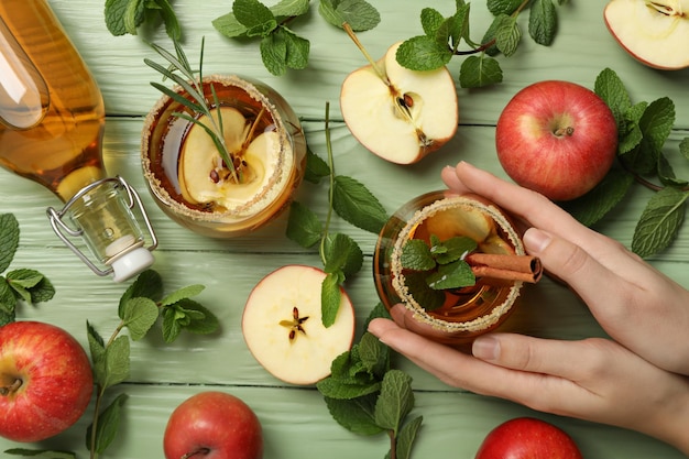 bicchieri e bottiglia con sidro di mela mele menta e mano su sfondo di legno verde vista superiore