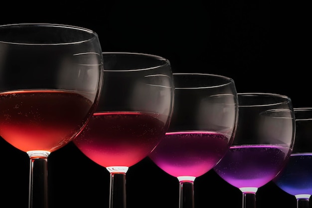 Bicchieri multicolori con diversi vini cocktail viola blu rosso su sfondo nero bicchieri di fila