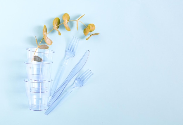 Bicchieri trasparenti in plastica blu con un ramo verde e forchette coltelli su sfondo azzurro