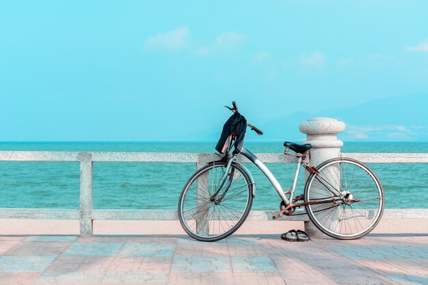 Bicicletta arrugginita con pantofole sul molo con vista sul mare blu.