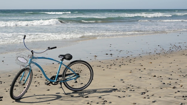Bicicletta blu, bici da crociera, costa della spiaggia dell'oceano, riva del mare della California USA. Ciclo su sabbia, onde d'acqua.
