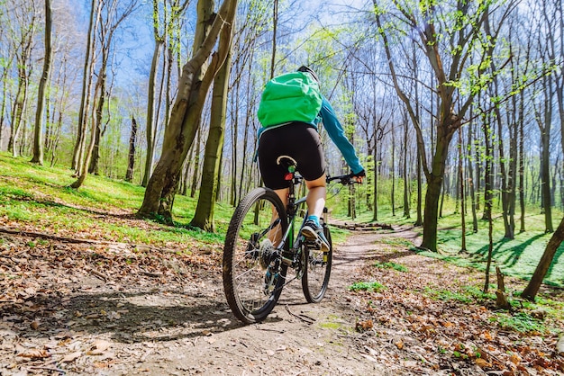 Bicicletta di corsa della giovane donna nella foresta dal sentiero