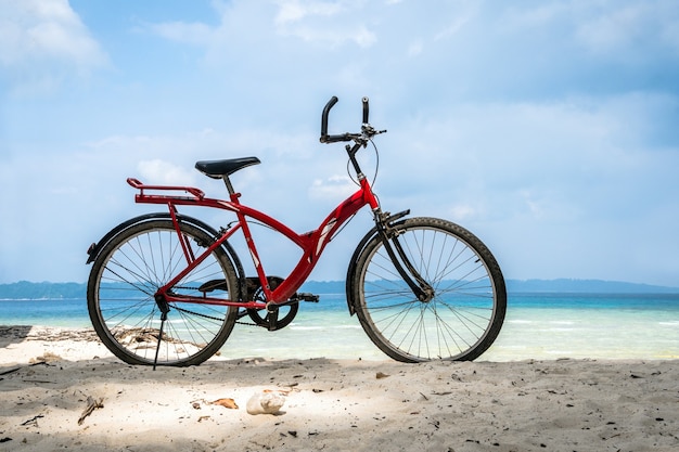 Bicicletta vintage rossa sulla spiaggia di sabbia bianca sul mare blu e sullo sfondo del cielo azzurro, concetto di vacanza primaverile o estiva. Bicicletta parcheggiata in riva al mare