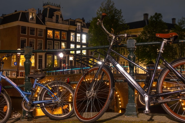 Biciclette per adulti e bambini sull'argine del canale ad Amsterdam di notte