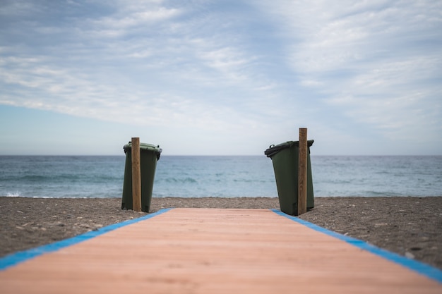 Bidoni della spazzatura alla fine di un sentiero in legno di fronte al mare. concetto di conservazione dell'ambiente.