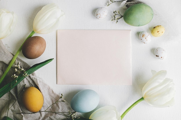 Biglietto d'auguri vuoto, eleganti uova di Pasqua, tulipani su piatto di legno bianco rustico con spazio per il testo