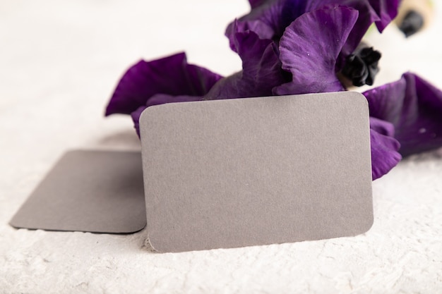 biglietto da visita grigio con fiori di iris viola su sfondo bianco cemento. vista laterale, copia spazio