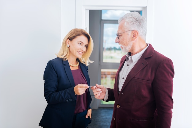 Biglietto da visita. Sorridente bella donna di affari che indossa un elegante costume blu che dà il suo biglietto da visita per un uomo influente