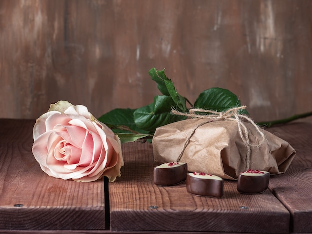 Biglietto di auguri con rosa, dolci e regalo in carta artigianale su vassoio in legno