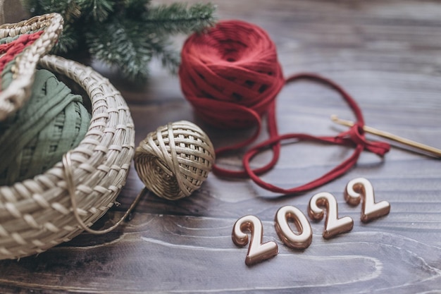 Biglietto di auguri di Natale e Capodanno 2022, gomitoli di filato lavorato a maglia, uncinetto e cesto lavorato a maglia su un tavolo di legno, vista dall'alto