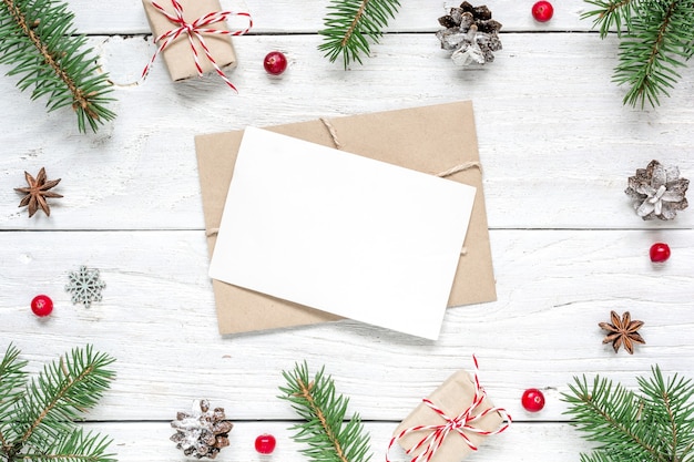 Biglietto di auguri di Natale in bianco nella cornice di rami di abete, bacche rosse, scatole regalo e coni