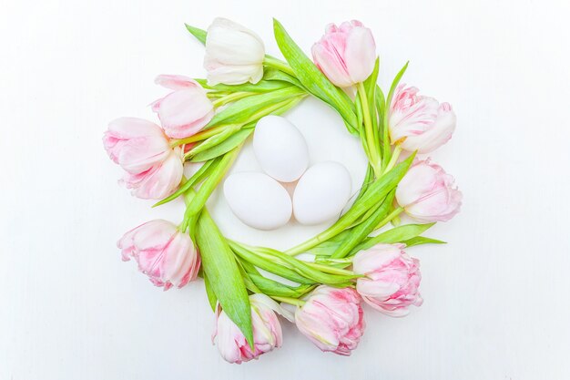 Biglietto di auguri di primavera. Uova di Pasqua nel nido e bouquet di fiori rosa tulipano fresco su fondo di legno bianco rustico