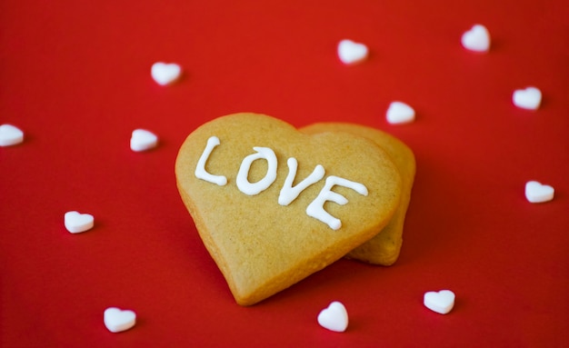 Biglietto di auguri di San Valentino, biscotti di pan di zenzero fatti in casa a forma di cuore con messaggio di AMORE e coriandoli di caramelle bianche sul rosso