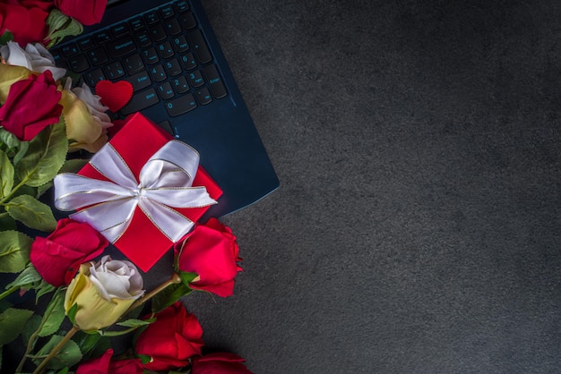 Biglietto di auguri di San Valentino con bouquet di fiori di rose rosse, vino e confezione regalo sul tavolo nero. Vista dall'alto con spazio per i saluti