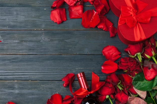 Biglietto di auguri di San Valentino. Fiori della rosa rossa, vino e contenitore di regalo sulla tavola di legno.