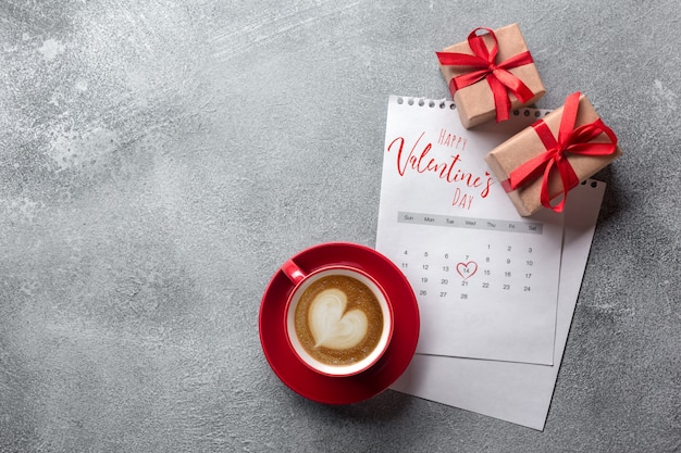 Biglietto di auguri di San Valentino. Tazza di caffè e contenitore di regalo rossi sopra il calendario di febbraio. Vista dall&#39;alto