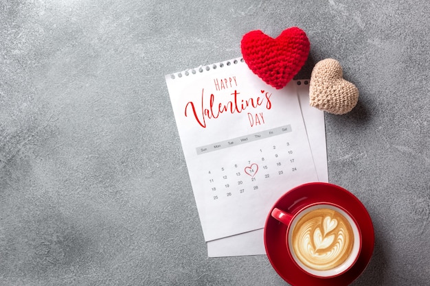 Biglietto di auguri di San Valentino. Tazza di caffè e contenitore di regalo sopra il calendario di febbraio sulla tavola di pietra.