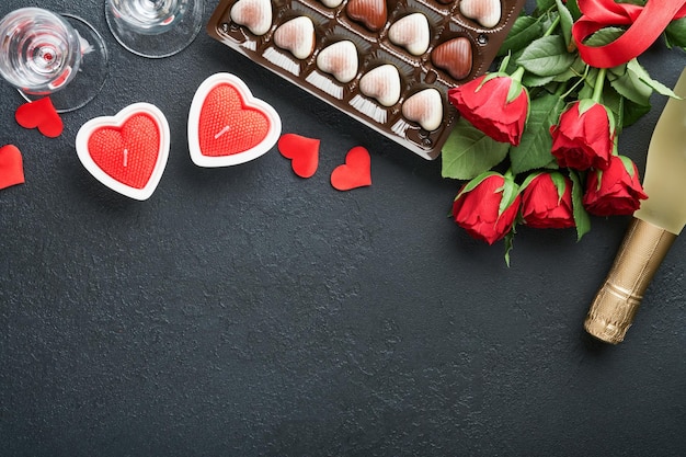 Biglietto di San Valentino Fiori rossi rosa biscotti brownie e caramelle al cioccolato su confezione regalo a forma di cuore con vino su sfondo nero Biglietto di auguri per la festa della mamma o della donna Vista dall'alto piatto