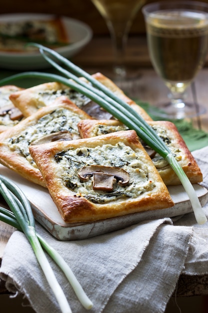 Bignè con formaggio, spinaci e funghi, serviti con vino e cipolle verdi. Stile rustico.