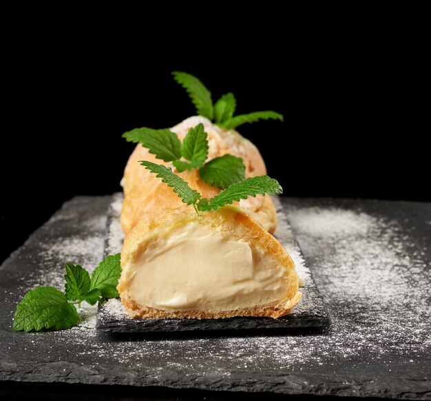 Bignè di crema pasticcera al forno e cosparsi di zucchero a velo e decorati con una foglia di menta su un bordo nero