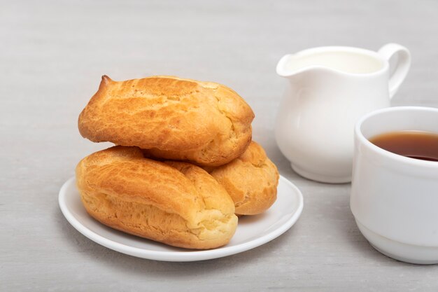 Bignè fatti in casa e tè con latte. Eclairs francesi tradizionali. Profiteroles sul piattino bianco.