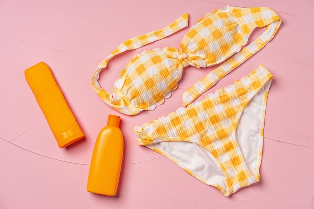 Bikini giallo con creme solari in rosa, piatto lay