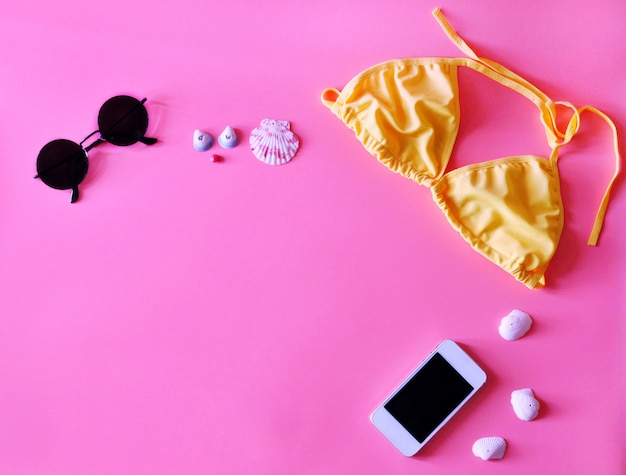 Bikini, occhiali da sole, smartphone e shell su sfondo rosa