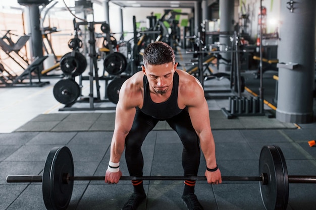 Bilanciere di sollevamento Il giovane uomo sportivo e forte in abbigliamento nero ha una giornata di allenamento in palestra