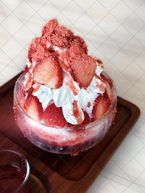 Bingsu di fragole in una tazza di vetro su un vassoio di legno.