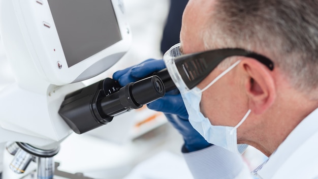 biologo scienziato in una maschera protettiva guardando attraverso un microscopio