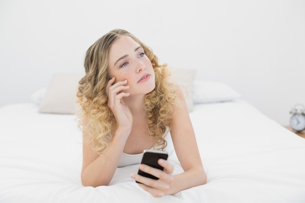 Bionda abbastanza premurosa che si trova sul letto facendo uso dello smartphone