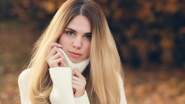 Bionda attraente in un maglione bianco su uno sfondo di colori autunnali