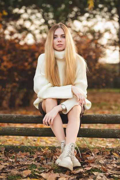 Bionda attraente in un maglione bianco su uno sfondo di colori autunnali